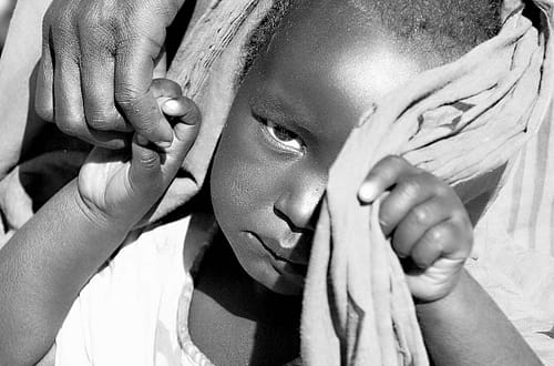 Flüchtling in Otash, Sudan. Kinderhände werden von einer Frauenhand gehalten. Das Kind ist sehr traurig. © Tom Rübenach
