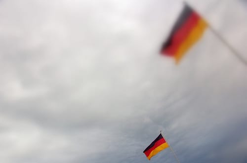Zwei Deutschlandfahnen ragen in den bewölkten Himmel, eine ist verwaschen und damit unscharf.